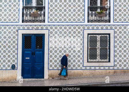 Ältere Frau, die an einem traditionellen Haus mit Azulejo-Fliesen vorbeikommt. Die Farbe Blau ist die vorherrschende Farbe in diesem Bild. Beja, Alentejo, Portugal Stockfoto