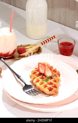 Einfache Croissant-Waffel oder -Croffle, serviert in rosafarbenem Teller mit Erdbeer- und Minzblatt-Topping, mit koreanischer Erdbeermilch Stockfoto