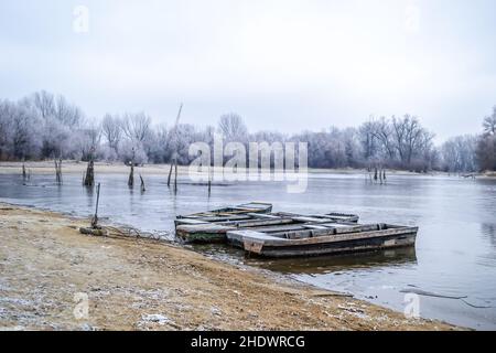 Vertäute Fischerboote aus Holz am Ufer des Donauzuges in gefrorenem Wasser. Stockfoto