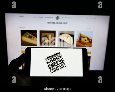 Person, die ein Smartphone mit dem Logo der Cheddar Gorge Cheese Company Limited auf dem Bildschirm vor der Website hält. Konzentrieren Sie sich auf die Telefonanzeige. Stockfoto