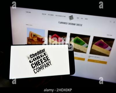 Person, die Mobiltelefon mit dem Logo des lokalen Käsemakers The Cheddar Gorge Cheese Company Ltd auf dem Bildschirm vor der Website hält. Konzentrieren Sie sich auf die Telefonanzeige. Stockfoto