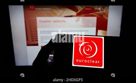 Person, die das Smartphone mit dem Logo der belgischen Finanzgesellschaft Euroclear Group auf dem Bildschirm vor der Website hält. Konzentrieren Sie sich auf die Telefonanzeige. Stockfoto
