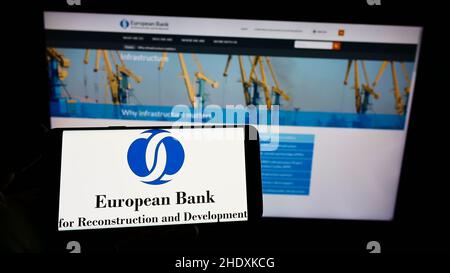 Person mit Mobiltelefon und Logo der Europäischen Bank für Wiederaufbau und Entwicklung (EBWE) auf dem Bildschirm mit Webseite. Konzentrieren Sie sich auf die Telefonanzeige. Stockfoto