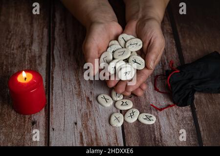 Frauenhände lehren Runen mit schwarzen Symbolen für Wahrsagerei auf einem Holztisch Stockfoto