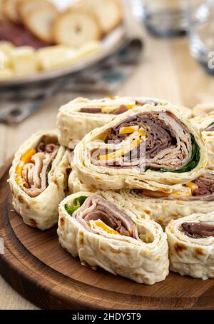 Tortilla-Wraps mit Roastbeef, pute, Käse und Salat auf einer Holzplatte gestapelt Stockfoto