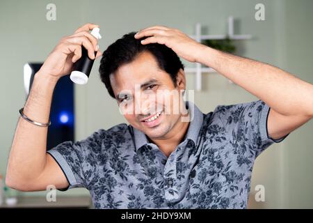 Junger, gutaussehender Mann, der Spray auf das Haar anwendet, indem er die Kamera anschaut - mit Haarauffrischer oder einer Behandlung zum Schutz des Haarausfalls. Stockfoto