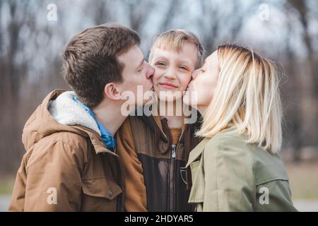 Kleinen Jungen Sohn in der Mitte übergeordnete Küssen in beiden Wangen. niedlich Familie Stockfoto