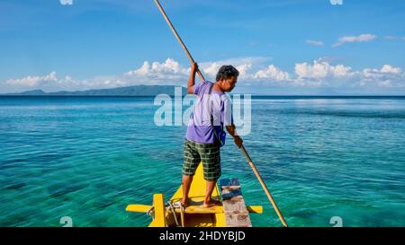 Puerto Galera, Philippinen - 26. November 2013. Ein philippinischer Bootsmann führt eine traditionelle banca mit einem Bambusstock durch flaches Wasser. Stockfoto