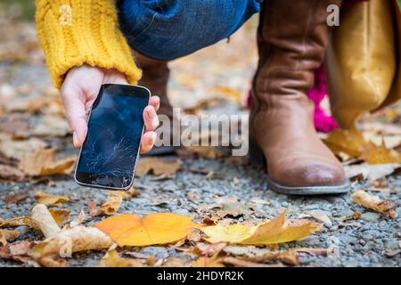 Frau, die ein beschädigtes Smartphone mit gesprungenem Touchscreen in die Hand nimmt. Defektes Smartphone in weiblicher Hand auf der Straße. Stockfoto