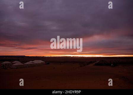 Touristische Zelte auf Sand in der Wüste gegen bewölkten Himmel in der Dämmerung Stockfoto