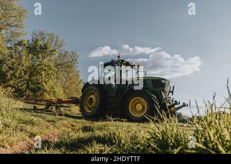 Blick aus der Perspektive des grünen Traktors, der das Heu während des sonnigen Mai-Tages teddelt Stockfoto