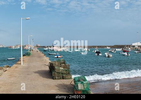 Der Fischerhafen von Sagres, Algarve, Portugal, mit einem langen Pier und geschützt durch eine riesige Meeresmauer. Hummertöpfe im Vordergrund Stockfoto