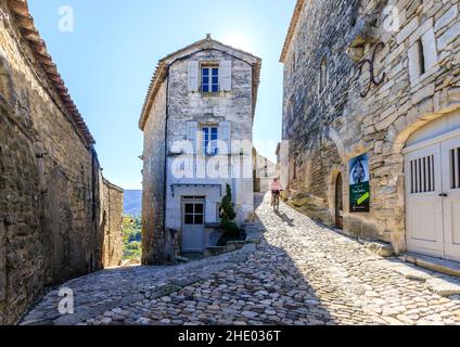 Frankreich, Vaucluse, Parc Naturel Regional du Luberon (Naturpark Luberon), Lacoste, gepflasterte Gasse im Dorf mit einem Radfahrer // Frankreich, VA Stockfoto
