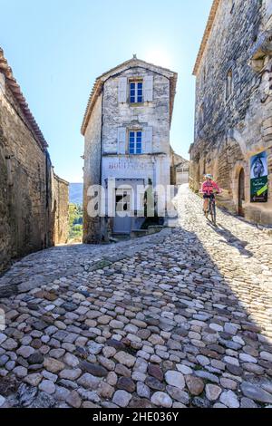 Frankreich, Vaucluse, Parc Naturel Regional du Luberon (Naturpark Luberon), Lacoste, gepflasterte Gasse im Dorf mit einem Radfahrer // Frankreich, VA Stockfoto