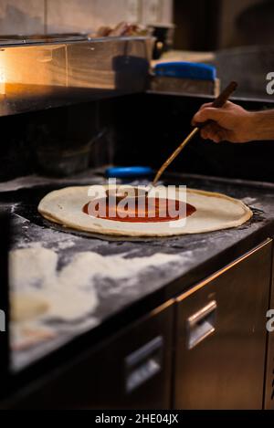 Mann, der in einer Küche Tomatensauce auf Pizzateig legt Stockfoto