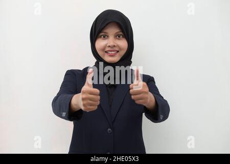 Junge asiatische muslimische Frau lächelt und macht OK Zeichen mit Handbewegung. Stockfoto