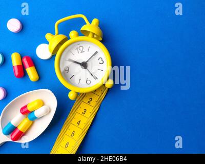 Löffel, Maßband, Uhr und Pillen Kapseln mit Kopierraum auf blauem Hintergrund. Selektiver Fokus. Stockfoto