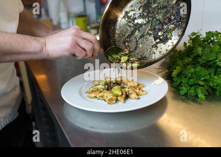 In einer Restaurantküche arrangiert der Küchenchef gegrillte Calamari auf einem Teller. Stockfoto