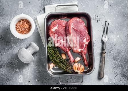 Rohe Tomahawk Kalbssteaks in Stahlblech mit Kräutern. Grauer Hintergrund. Draufsicht Stockfoto