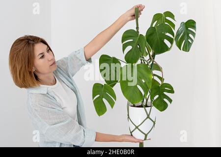 Handgemachte grüne Macrame-Pflanzenhänger mit Topfpflanze hängen an der Hand der Frau. Topf und Monstera-Pflanze Stockfoto