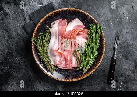 Roher, geschnittener Speck, fertig zum Kochen mit Kräutern. Schwarzer Hintergrund. Draufsicht Stockfoto