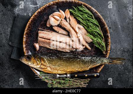 Heiß geräuchertes Heringsfischfilet auf rustikalem Teller mit Thymian und Rosmarin. Schwarzer Hintergrund. Draufsicht Stockfoto