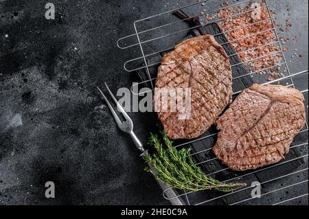 BBQ gegrilltes Rinderfleisch Sirloin Steaks auf dem Grill. Schwarzer Hintergrund. Draufsicht. Speicherplatz kopieren Stockfoto