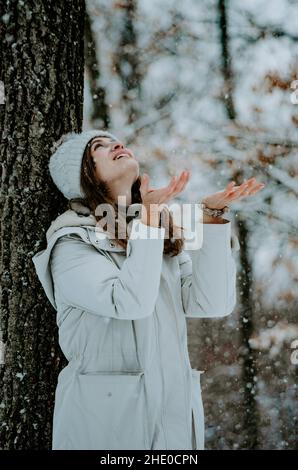 Vertikales Porträt einer Frau im Winterwald, die mit Palmen aufschaut, die Schneeflocken fangen. Konzept: Winterzauber, Verwunderung Stockfoto