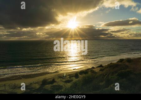 Sonnenuntergang über dem Meer, von einer Klippe aus gesehen, mit einem Sandstrand darunter Stockfoto