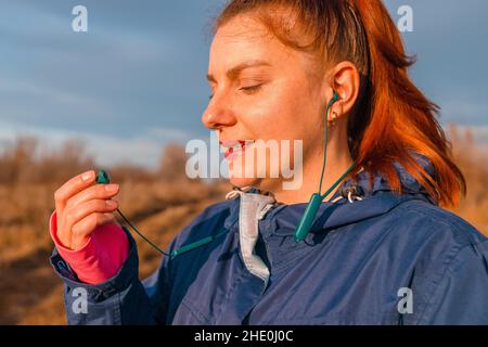 Die junge Sportlerin trägt Sportkopfhörer, um an einem sonnigen Herbsttag zu laufen. Vorbereitung auf den Marathon, Technologie. Stockfoto