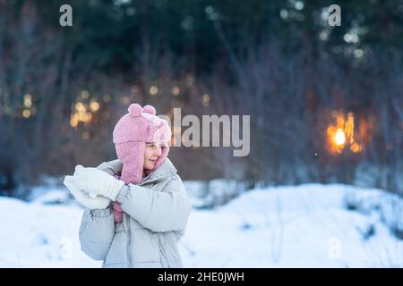 Nettes kleines Teenager-Mädchen mit Spaß spielen mit Schneebällen, bereit, den Schneeball zu werfen. Schnee-Spiele. Winterurlaub. Stockfoto