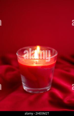 Eine rote Glaskerze auf rotem Satin-Hintergrund Stockfoto