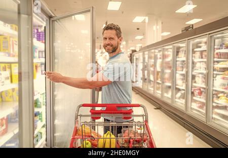 Glücklicher Mann mit Einkaufswagen, der Lebensmittel im Lebensmittelgeschäft kauft, einkaufen Stockfoto