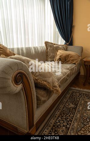 Komfortables und elegantes Sofa mit gemusterten Kissen, neben einem Fenster mit Vorhängen, Inneneinrichtung, Stoff- und Möbeldetails Stockfoto