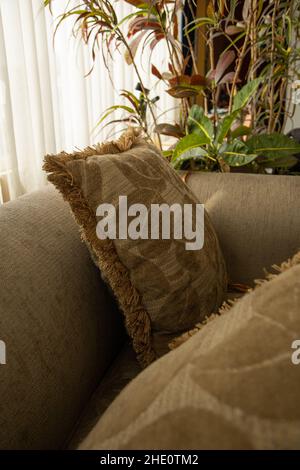 Detail der Textur von gemusterten Kissen auf einem Sofa, neben einem Fenster mit Vorhängen und einer Pflanze, häusliche Inneneinrichtung Stockfoto