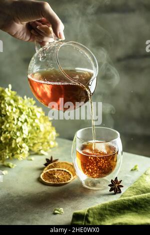 Zubereitung von Tee. Eine Tasse frisch geernteten Tee mit Blasen und Dampf auf strukturiertem Hintergrund mit Anissternen und getrockneten Orangenscheiben. Vertikale oris Stockfoto