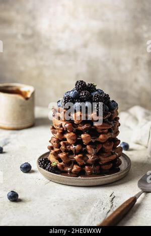 Köstlicher Stapel Schokoladenwaffeln mit Beeren und Schokoladensauce auf strukturiertem Hintergrund Stockfoto