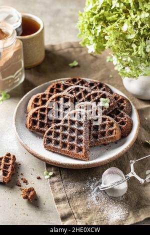 Herzförmige Schokoladenwaffeln als Valentinstag-Frühstück, bestreut mit Puderzucker Stockfoto