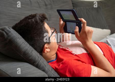 Kleiner Junge, der auf einem tragbaren Computerspiel spielt. Stockfoto