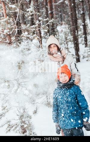 Mama und Sohn spielen Schneebälle im Winterwald. Mama geht mit ihrem Sohn bei Schneefall im Wald spazieren. Frohe Winterferien mit Schnee. Winterspaziergänge Stockfoto