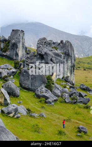 Eine in Rot gekleidete Touristenattraktion, die die Felsformationen von Castle Hill, Arthur's Pass, Neuseeland bewundert Stockfoto