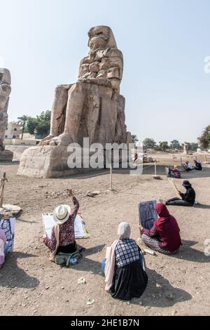 An der historischen Stätte Colossi of Memnon sitzen eine Gruppe ägyptischer Kunststudenten und zeichnen die antiken Statuen in ihre Skizzenblöcke. Stockfoto