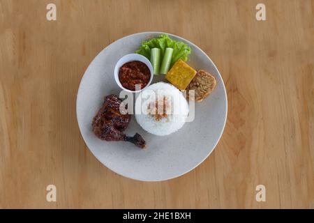 Pecel Ayam oder Ayam Penyet ist ein traditionelles indonesisches gebratenes Huhn mit frischem Gemüse, Chilisauce oder Sambal, Tofu und Tempeh Stockfoto