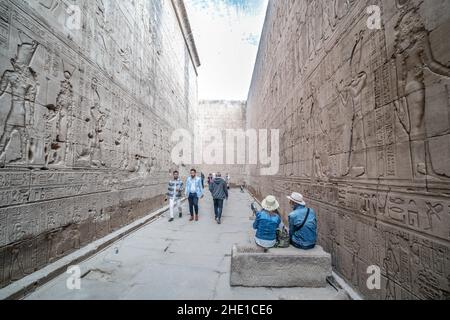 Ein reich eingeschriebener und geschnitzter Durchgang um den Edfu-Tempel, wo die Steinmauern dicht mit Hieroglyphen und Reliefskulpturen bedeckt sind. Stockfoto