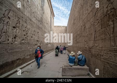 Ein reich eingeschriebener und geschnitzter Durchgang um den Edfu-Tempel, wo die Steinmauern dicht mit Hieroglyphen und Reliefskulpturen bedeckt sind. Stockfoto