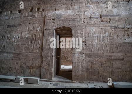 Eine kunstvoll verzierte Steintür, umgeben von alten ägyptischen Schnitzereien im Edfu-Tempel, Ägypten. Stockfoto