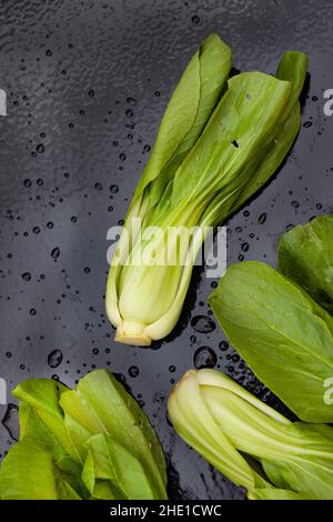 Frisch gewaschene rohe Bok Choy auf schwarzem Tisch mit Wassertropfen Stockfoto