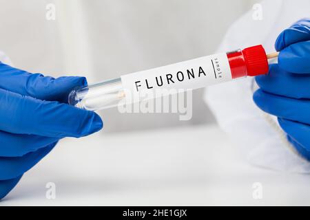 Medizinisches medizinisches medizinisches medizinisches Fachpersonal, das COVID-19 Abstrichbesteck hält, weißen PSA-Schutzanzug und Handschuhe trägt, Reagenzglas für die Einnahme von FLURONA Stockfoto