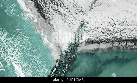 Meereslandschaftsfotografie, Winterlandschaft von oben fotografiert: Meeresstrand mit Flutwellen, schneebedeckter Strand und große Felssteine. Stockfoto