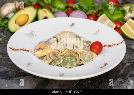 Tortellini mit Gemüse auf weißem Teller auf Marmortisch Stockfoto